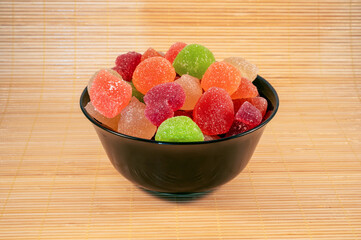 colorful candies in a black plate on a wooden background.