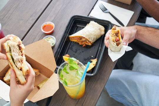 Friends eating takeout food at table sandwich and burrito with bites taken