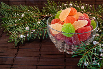 colorful jelly candies in a glass plate with christmas tree branches on a wooden background