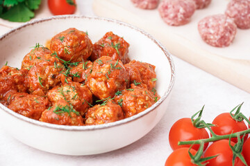 Bowl of tasty meat balls with sauce on light background