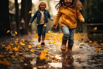 Fotobehang Happy little girl friends in jeans and rubber boots running through puddle on autumn day © sommersby