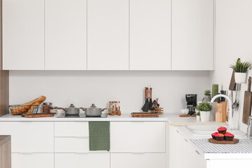 Interior of modern kitchen with white counters, cupboards and utensils