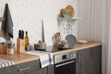 Wooden counters with plate rack, cutting board, utensils and electric stove in modern kitchen