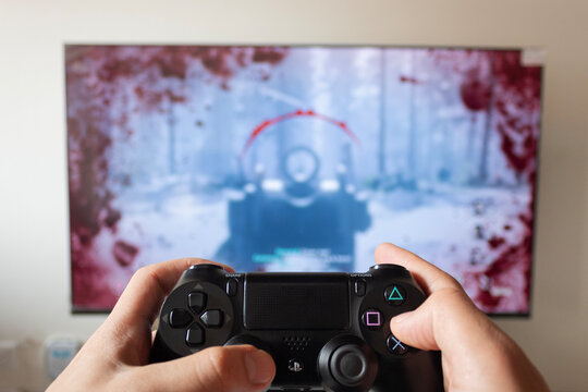 A male hand holding a play station 4 controller with call of duty world war video game in a smart tv at background