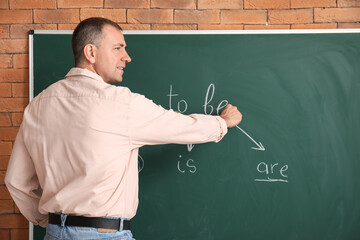 Male teacher writing English grammar on blackboard in classroom