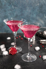 Glasses of Cosmopolitan cocktail with pomegranate and ice cubes on black table