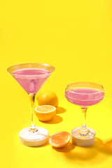 Glasses of Cosmopolitan cocktail with lemon on yellow background