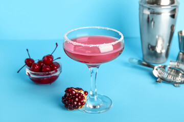 Glass of Cosmopolitan cocktail with pomegranate and cherries on blue background