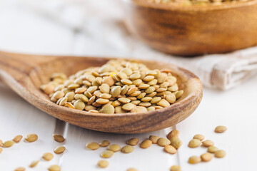 Uncooked lentil legumes in wooden spoon on white table.