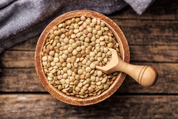 Uncooked lentil legumes in bowl on wooden table. Top view.