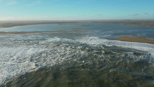 Aerial pan across sandbars at the mouth of the Orange River. Atlantic waves in foreground