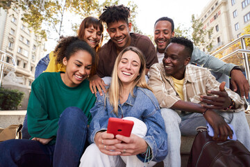Diverse group of university friends sitting on stairs in street city. Happy students using and...