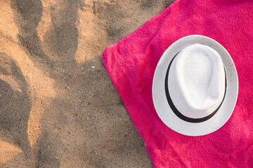 Bright towel with stylish straw hat on sand