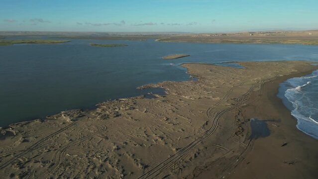 Fly over sandbank to reveal small flock of flamingoes standing in Orange River mouth estuary
