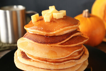 Plate of tasty pumpkin pancakes with honey on black background, closeup