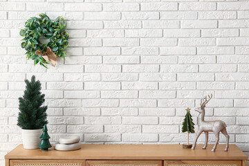 Wooden cabinet with Christmas decorations near white brick wall