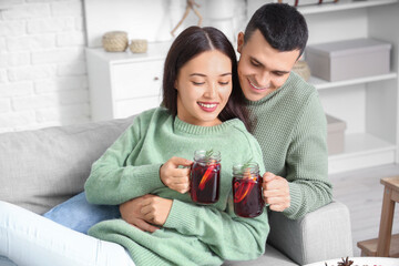 Happy couple with glasses of warm mulled wine lying on sofa in living room