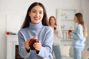 Pretty young woman with glass of warm mulled wine in living room at party