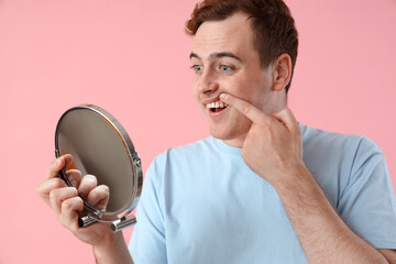 Young man with mirror on pink background, closeup