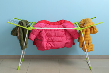 Clean puffer jackets hanging on dryer near blue wall