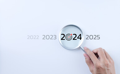 The 2024 new year business goals concept. A person holding a magnifying glass looking at the word...