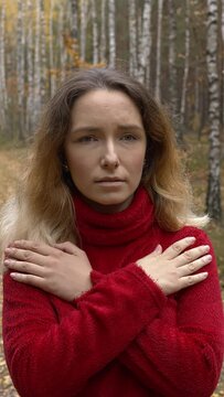 Female in red sweater  tapping her shoulders, crossing hands. Butterfly hug. Forest natural landscape. Vertical video.