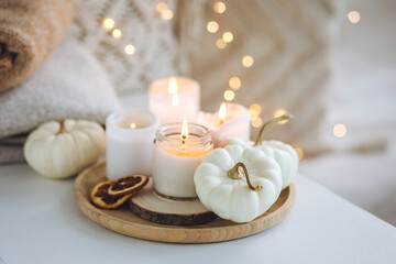 Fototapeta na wymiar Autumn home decor with white pumpkins and burning aroma candles with sweet spicy pumpkin pie scent. Cozy fall composition, relaxation, aromatherapy. Apartment design, living room or bedroom