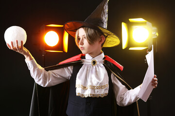 Little actor dressed as magician with film script on dark background