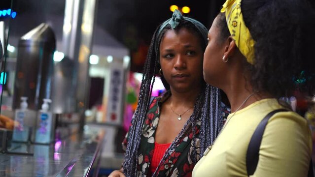 Happy young couple of lesbian Latinas women buying at fast food stand at outdoor fun fair. Two beautiful girls in love enjoying and having fun together. Cheerful and friendly people.