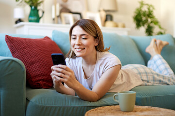 Happy woman text messaging on mobile phone while relaxing in the living room