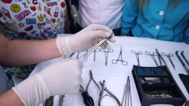 Teacher shows the usage of forceps and screwdriver at orthodontic practice. Multiple tools are on the stand. Close up.