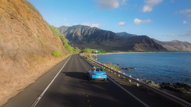 Aerial view sport car with tourist. Road trip, summer adventure. Beautiful nature of Hawaii tropical island in Pacific ocean. Blue convertible car driving on scenic road by West coast on Oahu island