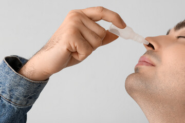 Young man using nasal drops on light background, closeup