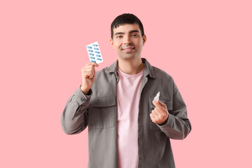 Young man with nasal drops and pills on pink background