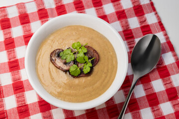 Cream mushroom soup in a yellow bowl on a red napkin. mushroom puree soup decorated with slices of fried mushrooms and a branch of fresh cilantro are on the table