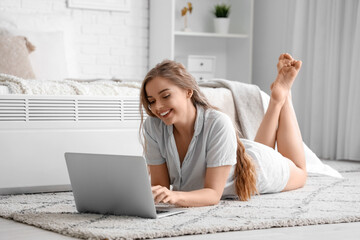 Young woman using laptop near radiator in bedroom - Powered by Adobe