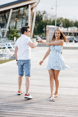 Fototapeta premium A couple in love, a man and a woman, walk along a wooden pier. A man and a woman hold hands and run along a wooden pier. Stylish man and his beautiful woman smiling and having fun