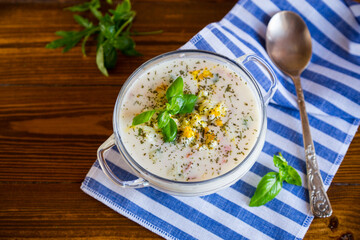 Cold soup with cucumbers, eggs, vegetables, yogurt and fresh herbs in a glass bowl .