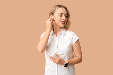 Pretty young woman with wireless earbuds on beige background