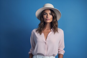 Portrait of beautiful young woman in hat and shirt on blue background