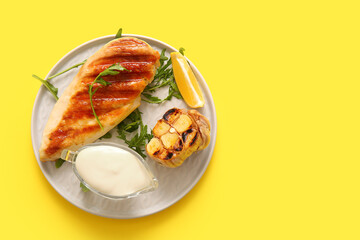 Plate of tasty grilled chicken breast with arugula, garlic and mayonnaise on yellow background
