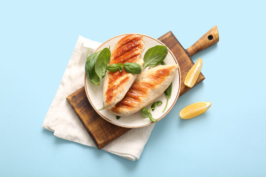 Plate of tasty grilled chicken breast with basil and lemon on blue background