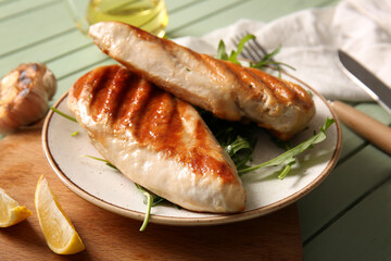 Plate of tasty grilled chicken breast with arugula, garlic and lemon on green wooden background