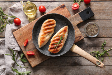 Frying pan of tasty grilled chicken breast with rosemary and tomatoes on wooden background