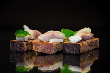 canape of pieces of salted herring with onions on a fresh dark piece of bread.