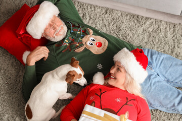 Obraz premium Happy mature couple with dog and gift lying at home on Christmas eve, top view