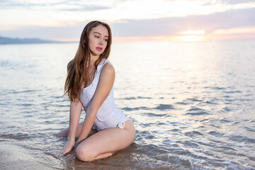 Fototapeta na wymiar Sexy girl sitting at sand at sea shore at sunset