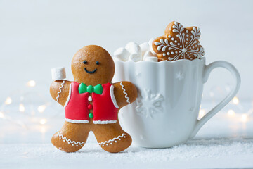 Christmas card with a gingerbread man and a mug with marshmallows on a wooden table and a white background, a light garland