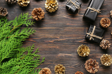 Frame made of pine cones with Christmas gift boxes and coniferous branches on wooden background