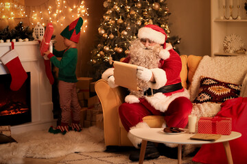 Santa Claus reading letter with cute little elf at home on Christmas eve